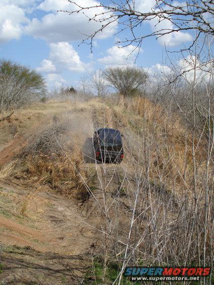 Dark SUV kicking up dust on a dirt path in a dry, brushy area