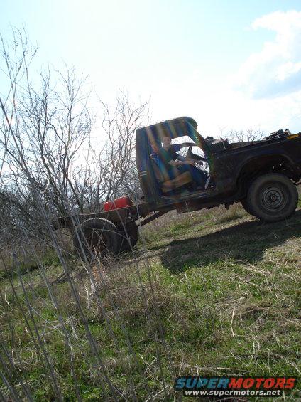 Two people sit in the cab of a derelict truck chassis with a red fuel tank visible