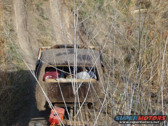 Mud-covered off-road vehicle with items in the back, seen from above and behind