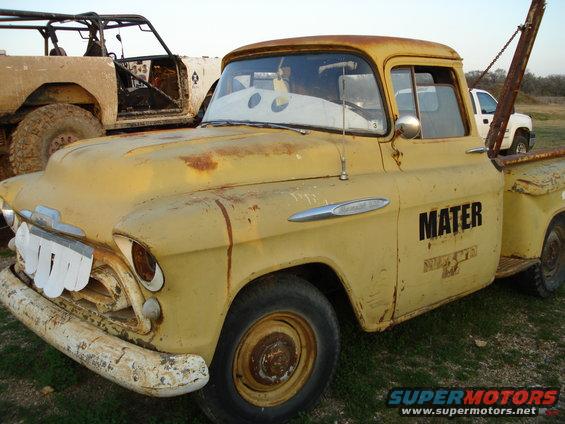 Yellow tow truck, possibly a 1955 Chevrolet, with "MATER" on the door and cartoon eyes on the windshield. Another off-road vehicle is behind it