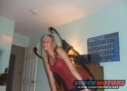 Woman in a red tank top wearing large, dark wings. A poster is on the wall behind her
