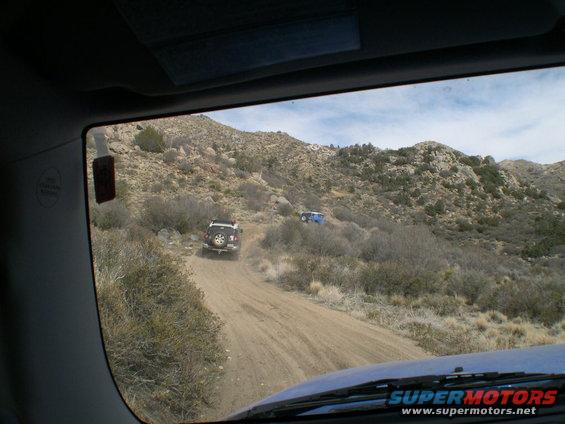 Two SUVs driving up a dusty mountain road. One is dark colored, the other is blue