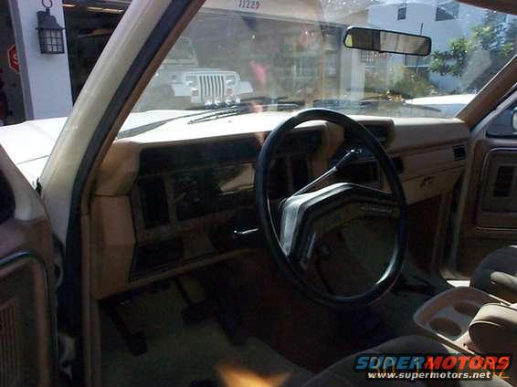 Interior of a 1980s SUV, showing dashboard and steering wheel. Another vehicle is visible through the windshield