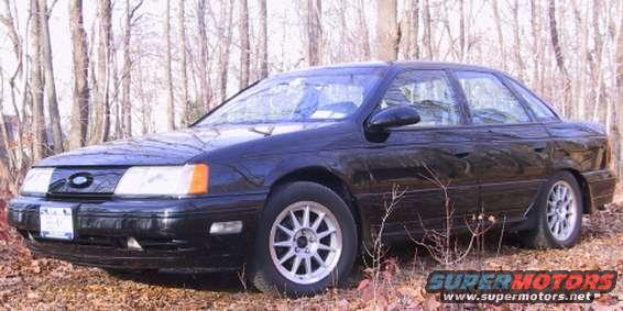 1989 Ford Taurus sedan, black, parked outdoors with trees in background