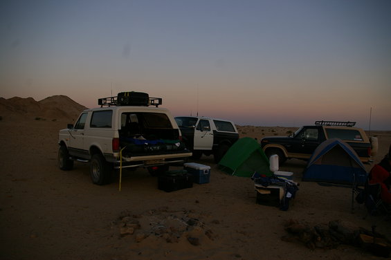 Three Ford Broncos parked at a desert campsite with tents and gear