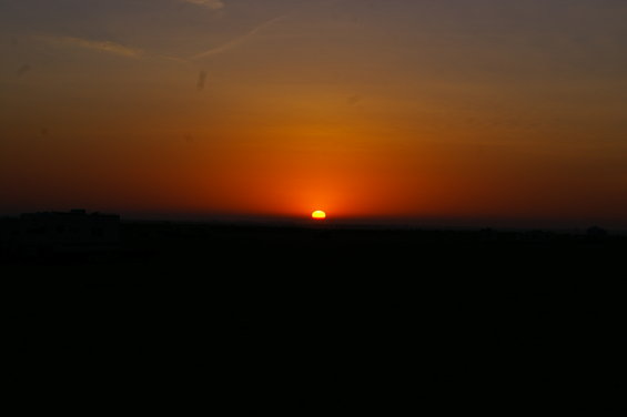 sun setting on the horizon with orange and purple sky over a dark silhouette of land