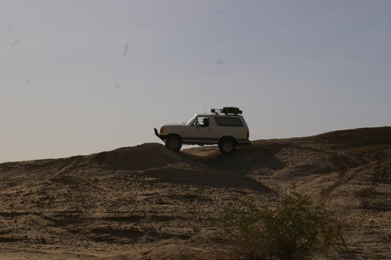 1986 Ford Bronco driving on a dirt hill with a roof rack