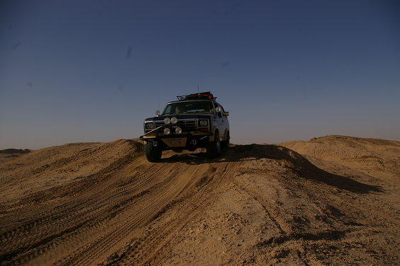 Dark SUV with off-road lights and roof rack driving on sand dunes