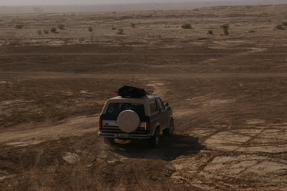 1986 Ford Bronco driving on a dirt road in a desert landscape