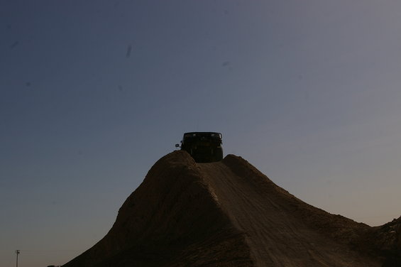 Dark SUV on top of a dirt mound against a clear blue sky