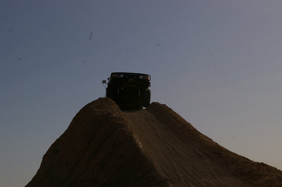 Dark 1986 Ford Bronco cresting a dirt hill against a clear sky
