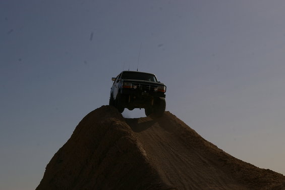 Dark-colored 1987 Ford F-150 climbing a dirt mound against a clear sky