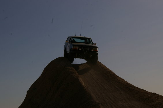 Ford Bronco driving up a dirt mound against a clear sky