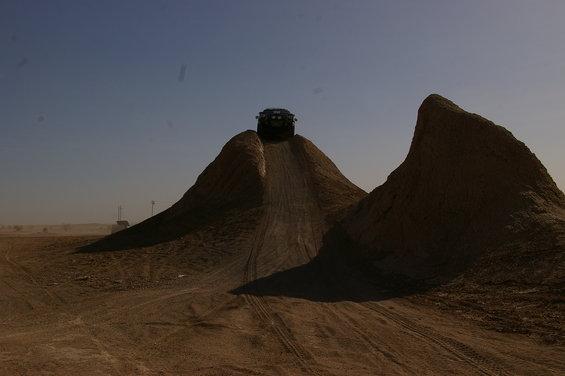 Dark SUV cresting a dirt mound against a clear blue sky