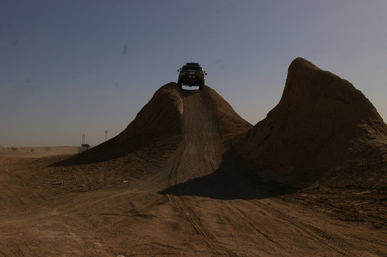 Dark SUV with roof rack cresting a dirt hill under a clear blue sky