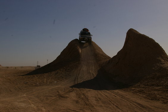 White SUV cresting a dirt hill with luggage on roof