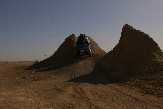 Van with luggage on roof driving up a dirt hill in a desert landscape