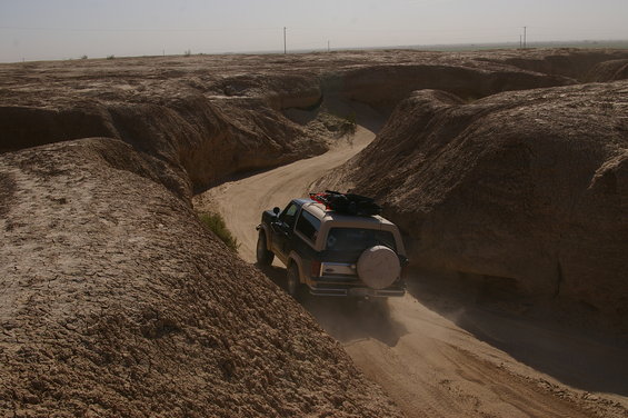 Ford Bronco driving on a dusty, winding dirt road through a desert canyon