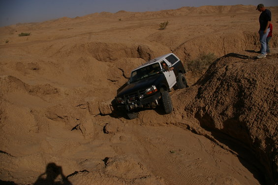 SUV driving down a steep sandy slope with a person watching from above