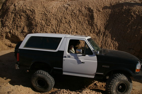 Black and white Ford Bronco with off-road tires parked on sandy terrain