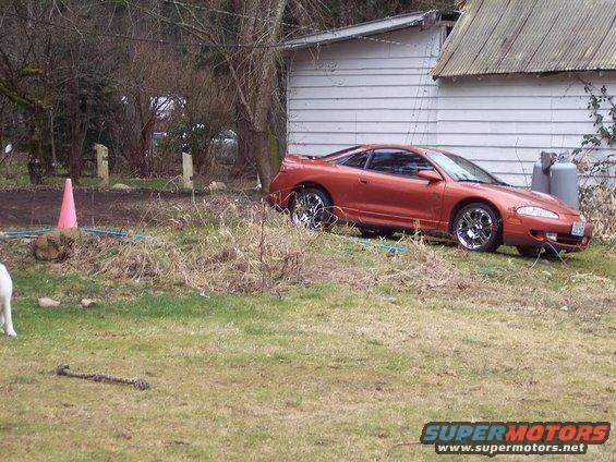 Orange 1995 Mitsubishi Eclipse coupe parked on grassy area next to a white building