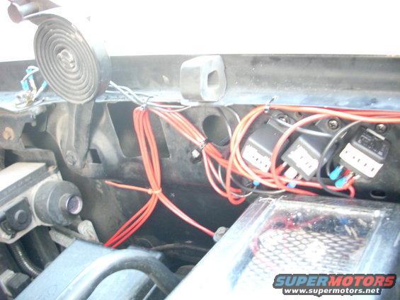 Engine bay with red wires, relays, and a coiled spring