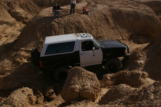 Two-tone black and white Ford Bronco off-roading on a sandy hill, with "98" visible on the roof