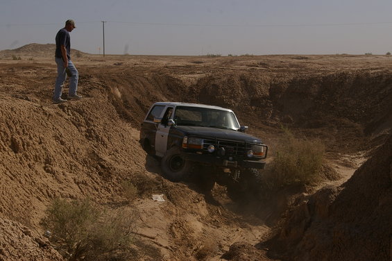 Man watches a dark blue and white Ford Bronco drive down a dirt ravine