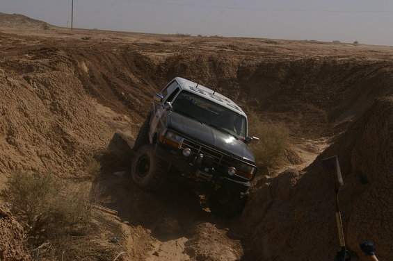 Dark blue and white Ford Bronco navigating a dirt ravine, front winch visible