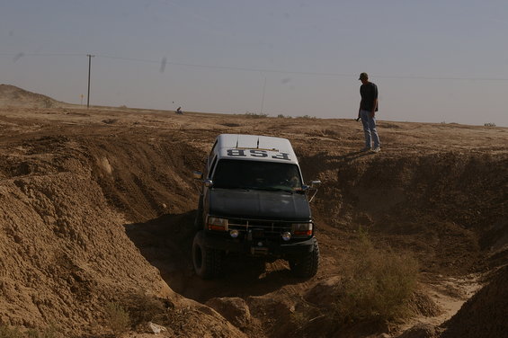 SUV driving down a steep dirt path, person watching from above