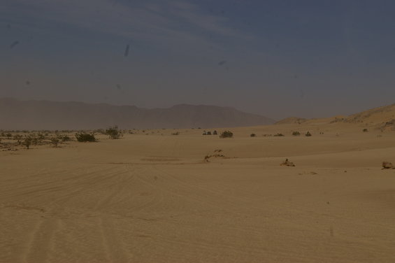 Desert landscape with tire tracks in sand and distant mountains under a hazy blue sky