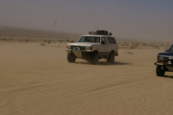 white SUV with roof rack driving in desert, another dark SUV to the right
