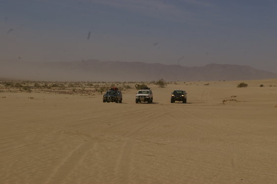 Three SUVs driving on sand dunes under a hazy sky