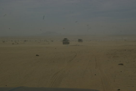 Two SUVs driving on a sandy track in a hazy desert landscape