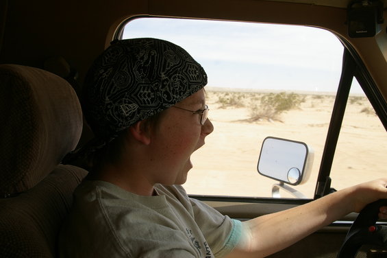 Person wearing a bandana and glasses driving a vehicle through a desert landscape