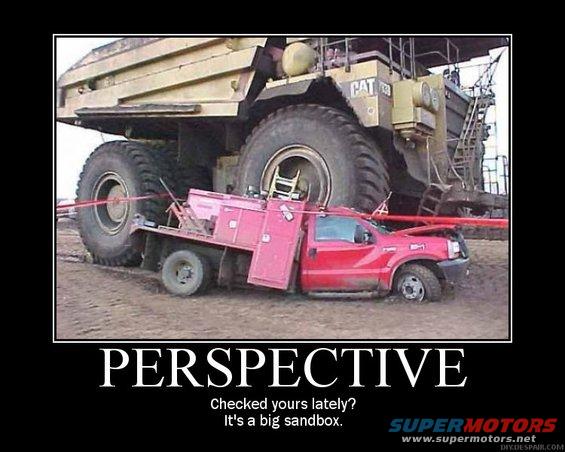 Red pickup truck stuck in dirt next to a massive yellow mining truck's tire
