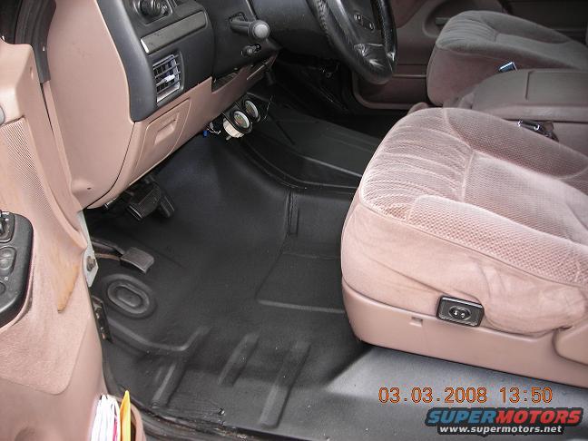 Interior of a 1990s Ford Bronco showing tan seats, black floor mats, and dashboard details