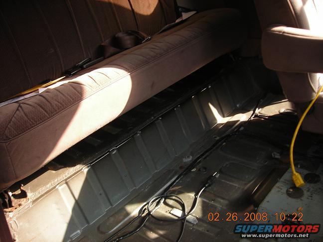 Interior of a vehicle with rear seat and carpet removed, showing floor pan and wiring