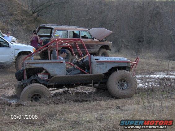 Custom off-road buggy stuck in mud, with a brown SUV behind it