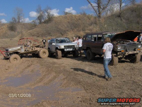 four off-road vehicles stuck in mud, one with hood open