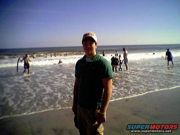 guy in a green shirt and hat on a beach with people in the ocean