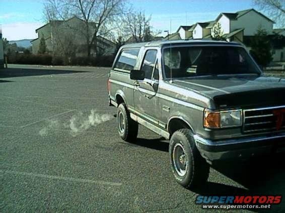 Gray Ford Bronco parked on asphalt, exhaust smoke coming from the side