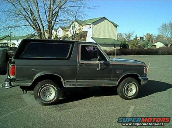 Dark gray 1987 Ford Bronco SUV parked on asphalt, side view, with a spare tire on the rear