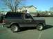 1989 Ford Bronco - A dark gray Ford Bronco is seen from the side, parked in an outdoor lot with buildings in the background.
