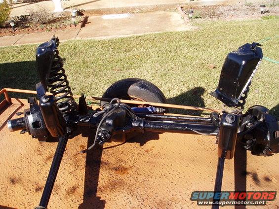Black front axle assembly with coil springs and shock mounts on a metal trailer