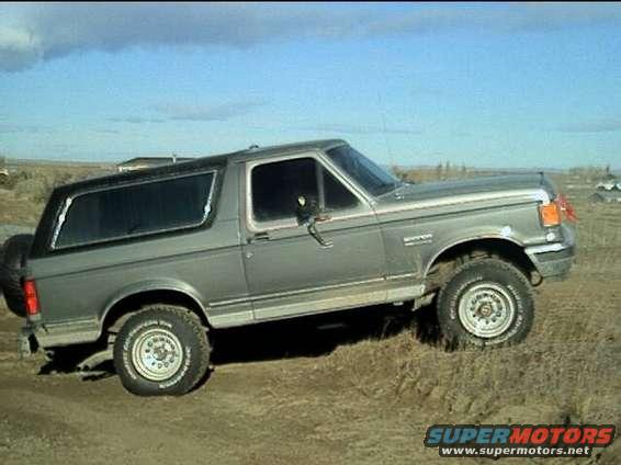 1989 Ford Bronco parked on dirt with a spare tire on the back