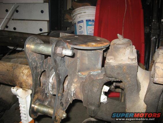 Close-up of a welded suspension component attached to a vehicle axle, supported by a jack stand