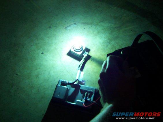 hand holding flashlight over car battery with visible wires and terminals