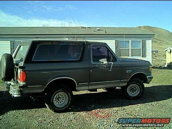 Dark gray Ford Bronco with a spare tire on the back, parked on gravel