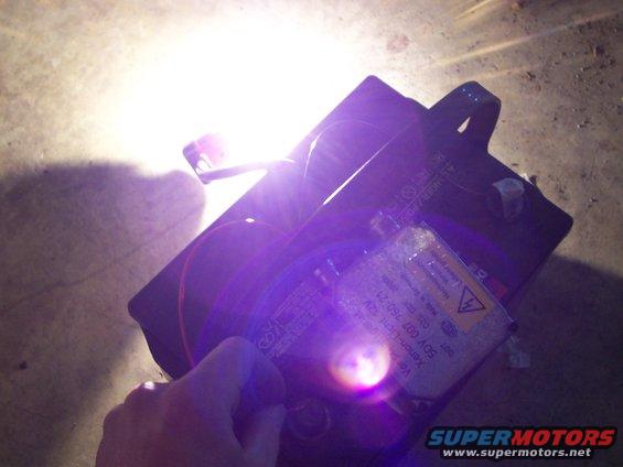 Hand holding a car headlight ballast with visible text and a bright light source